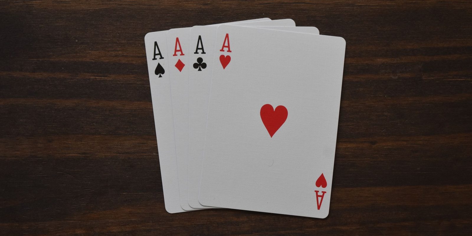 Four aces fanned on a dark wooden table — the PromoLineup house deck